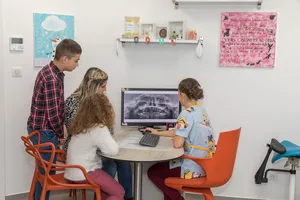 La praticienne montre une radiographie panoramique à trois enfants assis autour d’une table