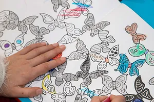 Des mains d’enfant colorient un dessin de papillons dans la salle d’attente
