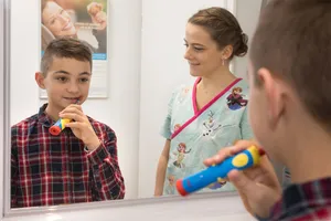Un garçon apprend à se brosser les dents devant un miroir, guidé par la praticienne