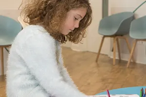 Une enfant dessine, assise dans la salle d’attente du cabinet