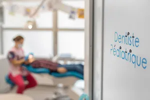 La mention « Dentiste Pédiatrique » sur la vitre, la salle de soins en arrière-plan